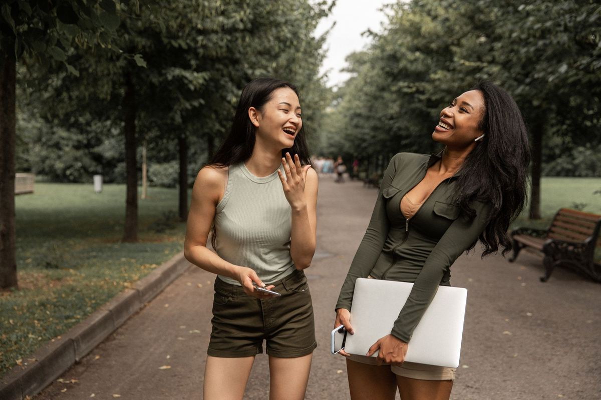 Two young women talking and laughing on a path through a park